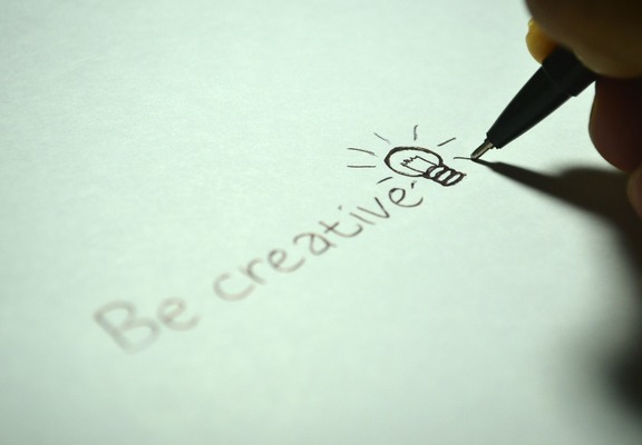 A person holding a marker pen writing, ‘be creative’ and drawing a light bulb