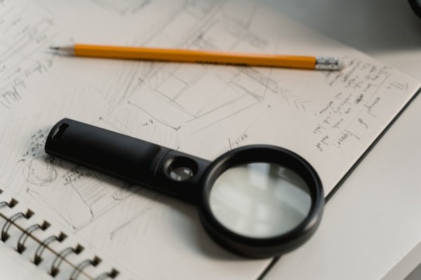 Black magnifying glass and yellow pencil placed on writing pad