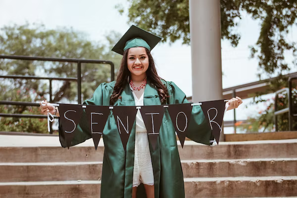 picture of a triumphant female student holding up a 'Senior' sign during her graduation